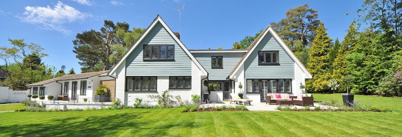 Large detached suburban house with a wide green lawn, blue sky, and landscaped front yard