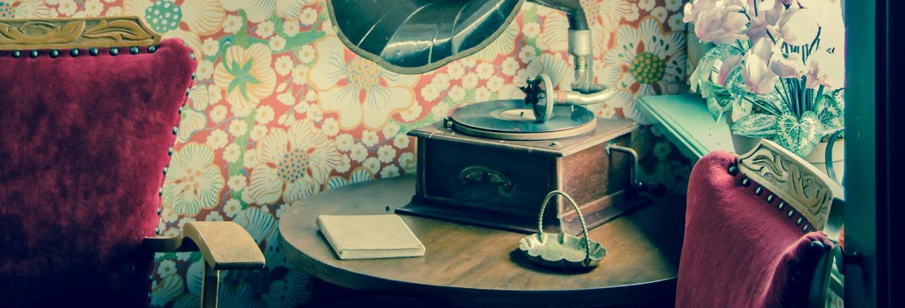 Antique gramophone displayed on a table beside a vase of flowers with floral wallpaper and a red chair, representing careful handling by antique moving services fort lauderdale fl