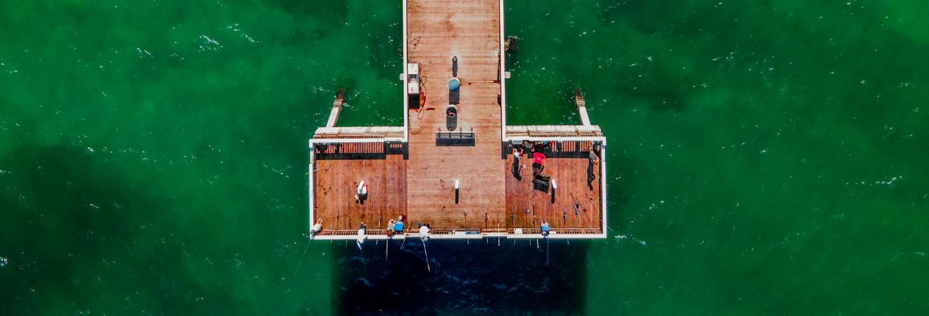 Aerial view of a long wooden pier with a covered center section over bright green coastal water