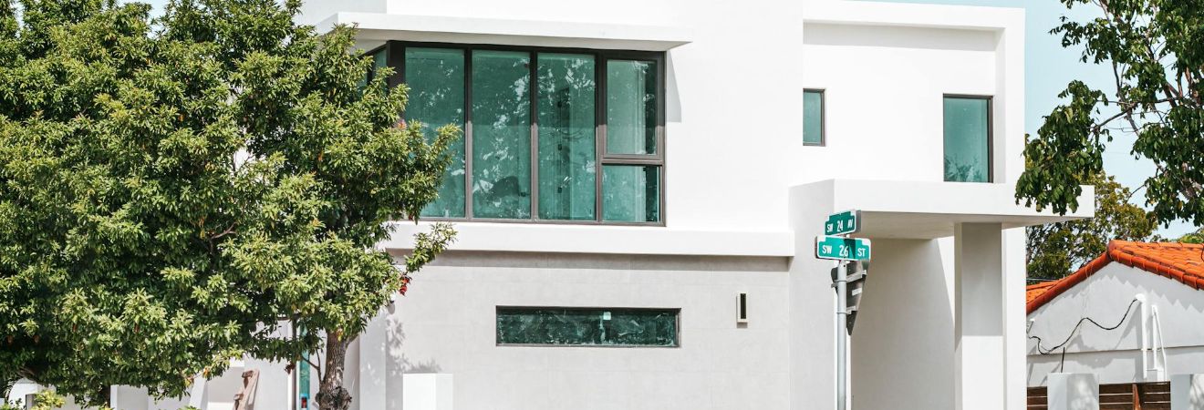 Modern white two-story house on a quiet corner lot with large windows and trees around the property where movers Broward County will relocate someone