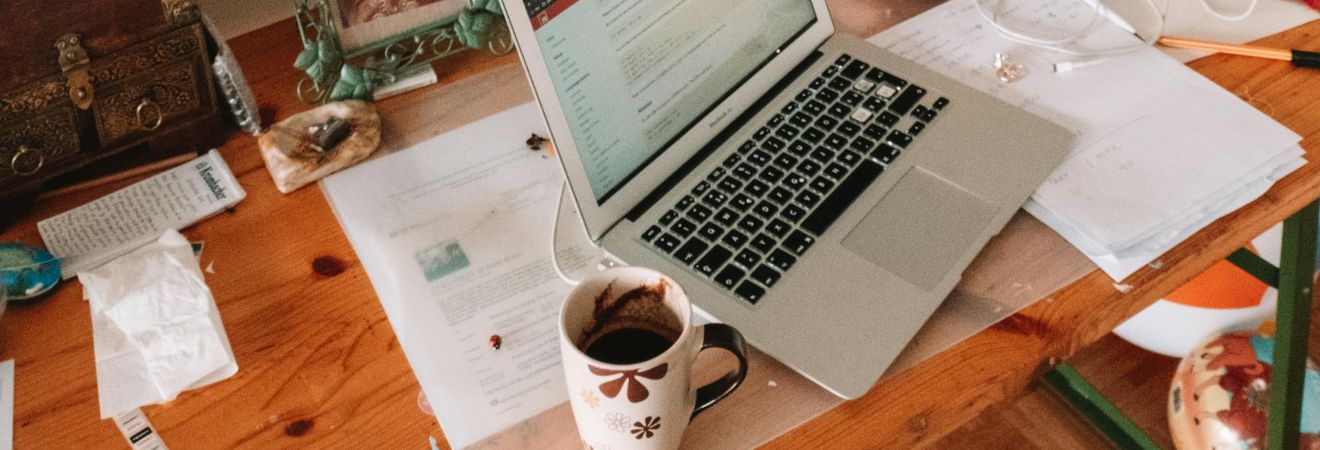 a laptop and a coffee mug on a wooden table with some clutter around it